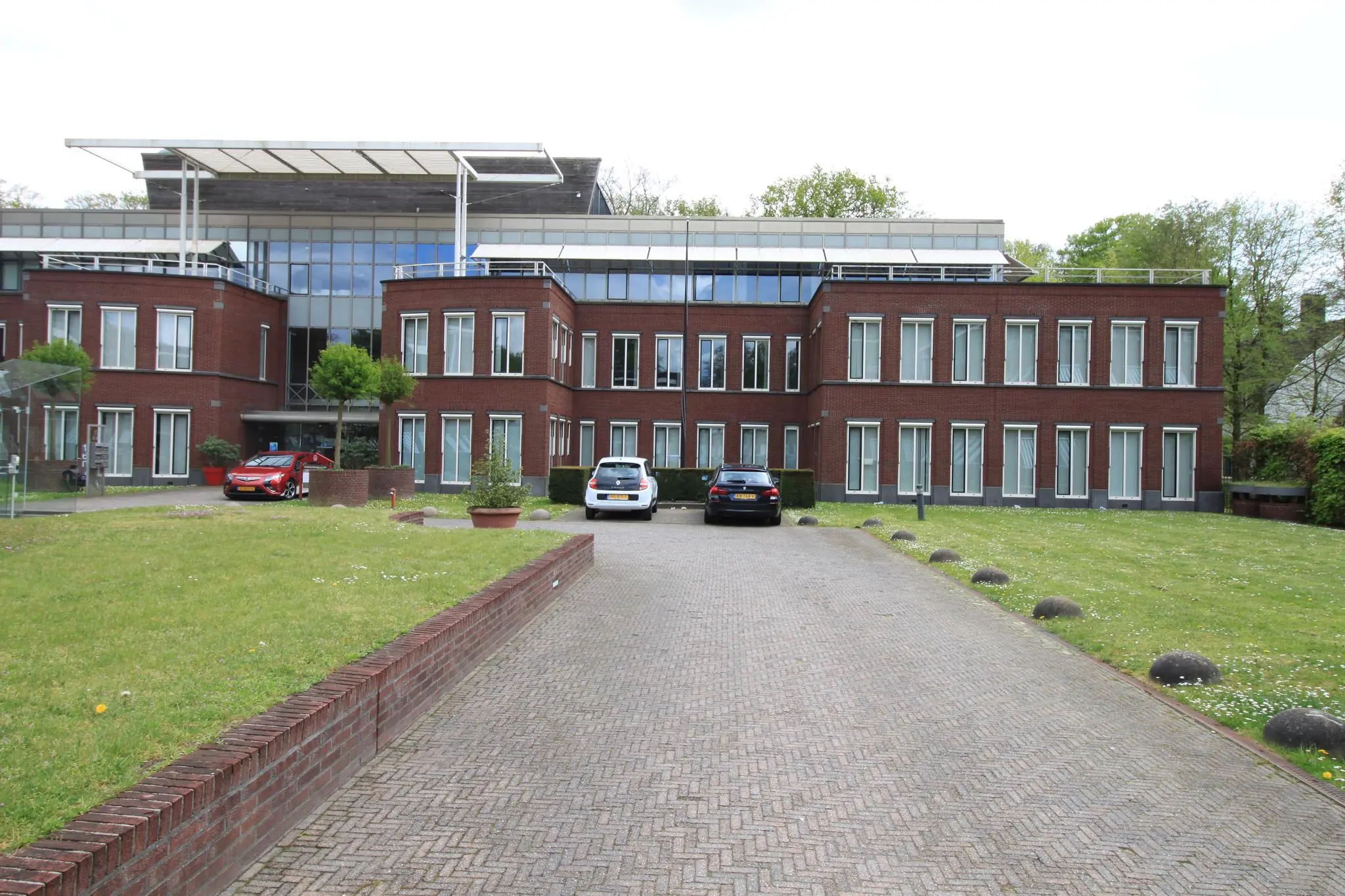 Modern kantoorgebouw aan de Arnhemse Bovenweg met een rode bakstenen gevel en geparkeerde auto's op de oprit.